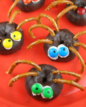 Four chocolate spider donuts on an orange plate.