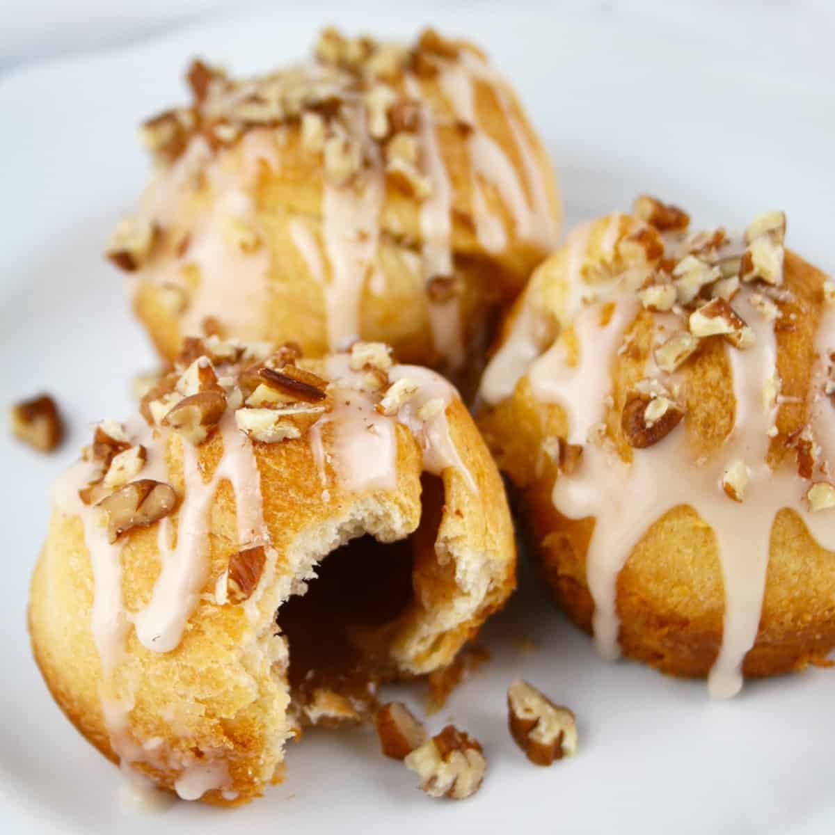 Three cinnamon sugar rolls on plate, one with a bite taken out showing hollow center.