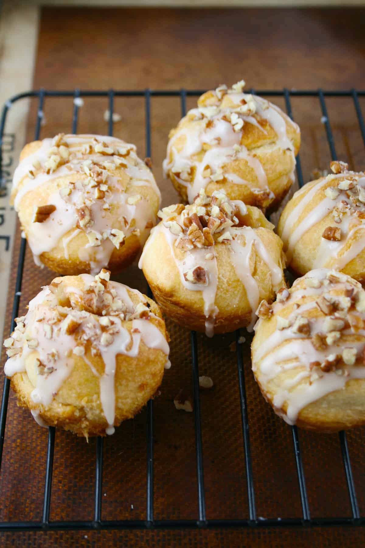 Baked and frosted cinnamon sugar rolls (six) on cooling rack with nuts on top.