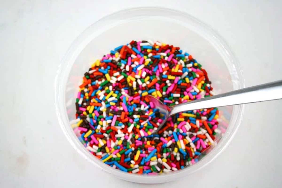 a bowl of multicolored sprinkles in a clear bowl with a spoon inside.