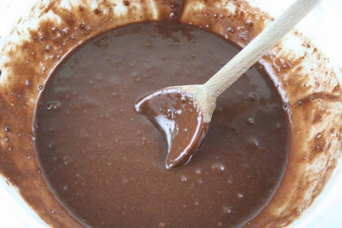 mixed brownie batter in white bowl with wooden spoon in batter.
