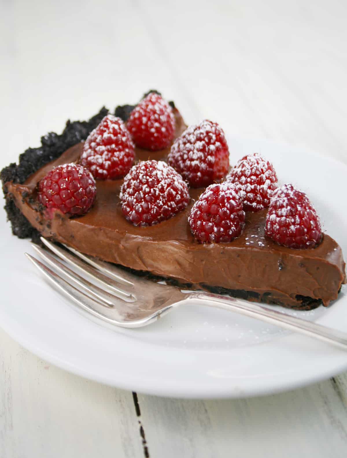 Slice of chocolate tofu tart with raspberries on a plate.