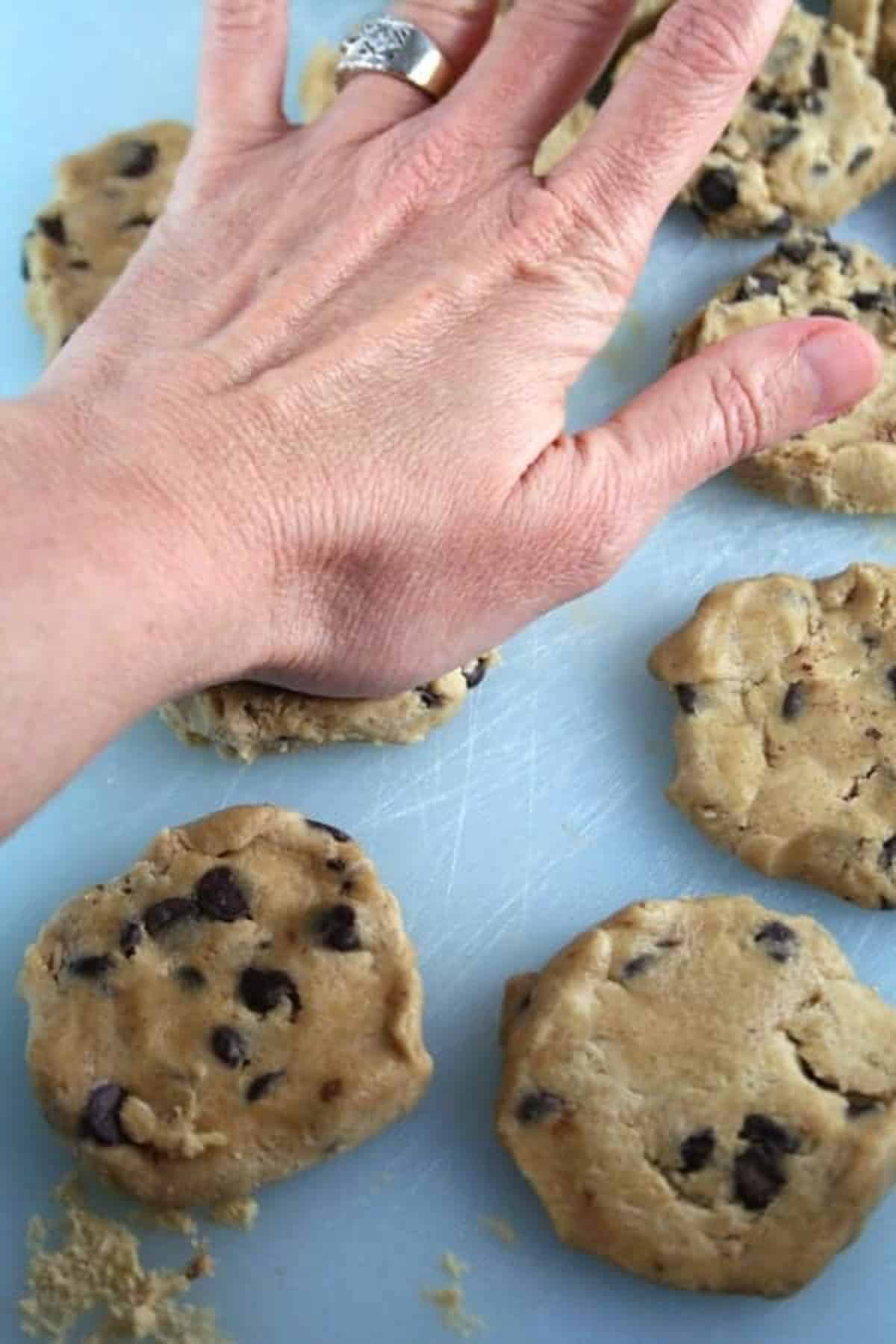 hand pressing down chocolate chip cookie dough. 