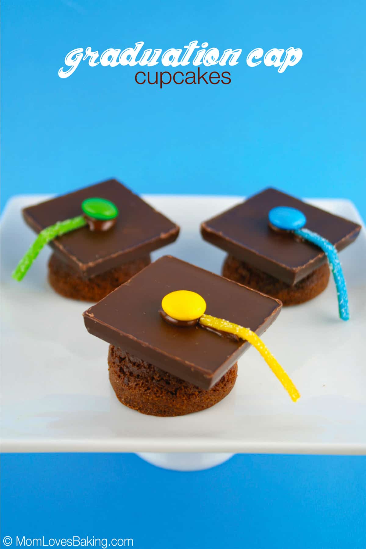 Three brownie bites with chocolate squares to look like graduation caps on a white plate with blue background.