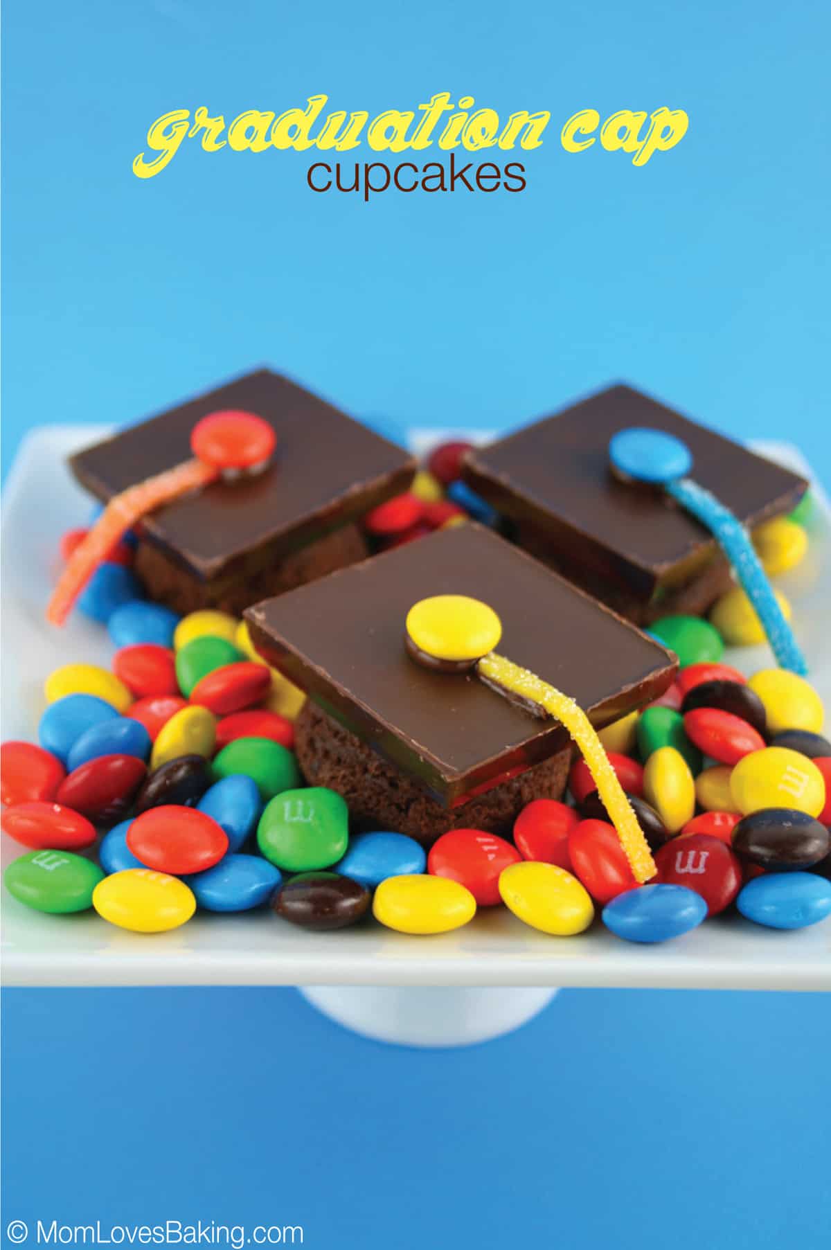 3 brownie bites decorated to look like graduation caps on a white plate and lots of M&M candies on the plate too.