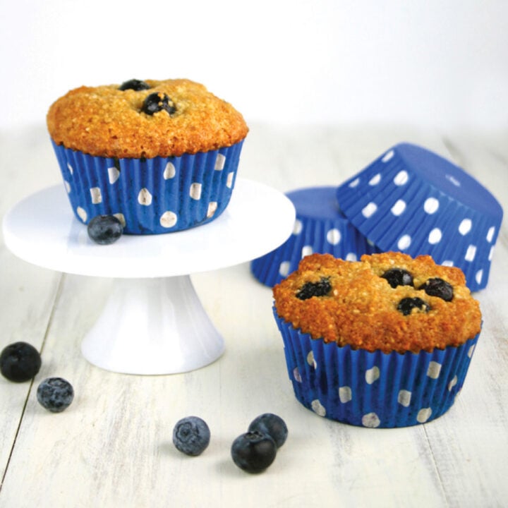Two paleo orange blueberry muffins a white kitchen counter.