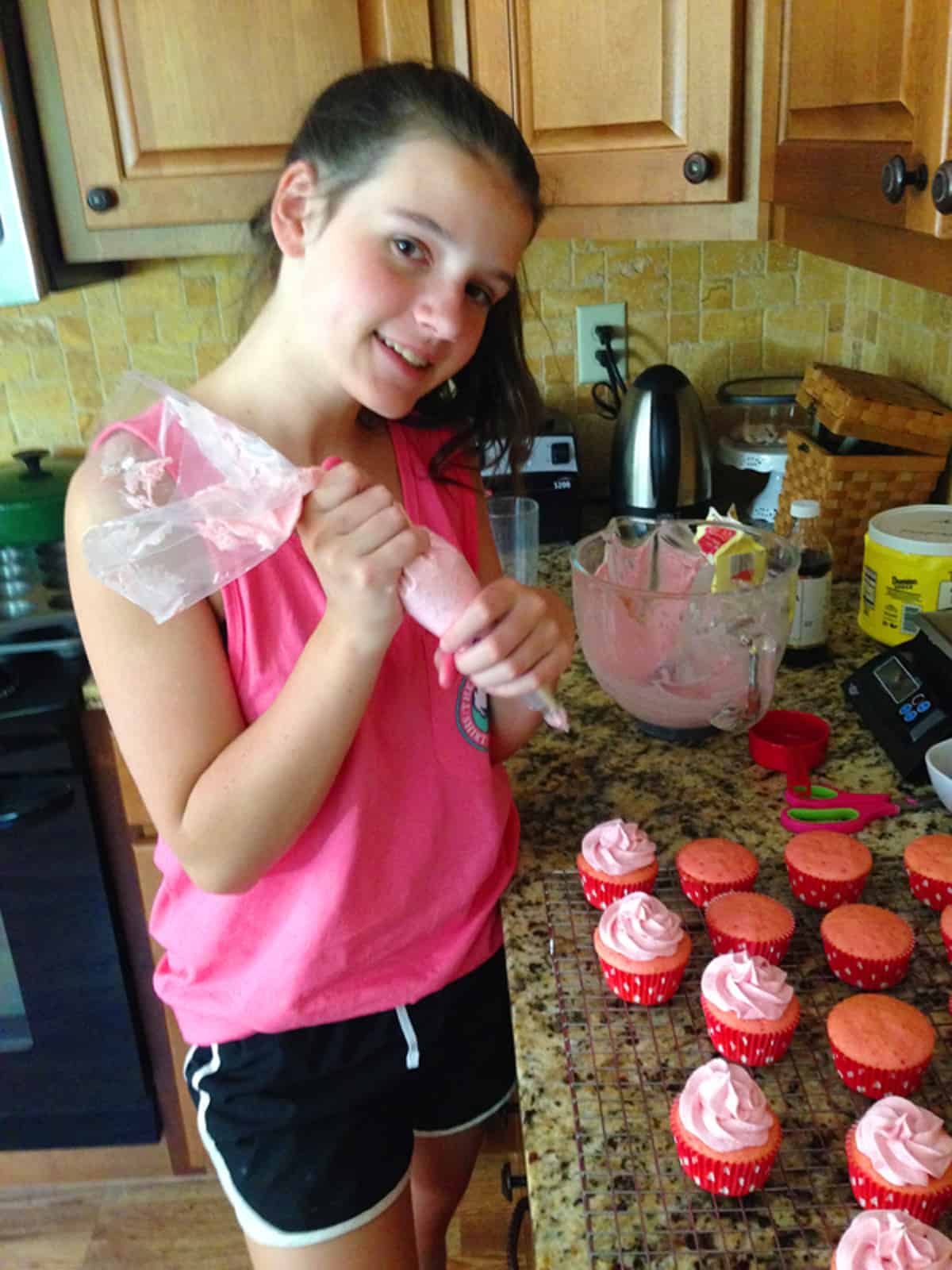 Girl decorating strawberry cupcakes in the kitchen.