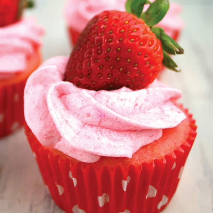 Close up of one strawberry cupcake with pink frosting and strawberry on top.