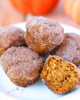 Five mini pumpkin muffins on a white plate.