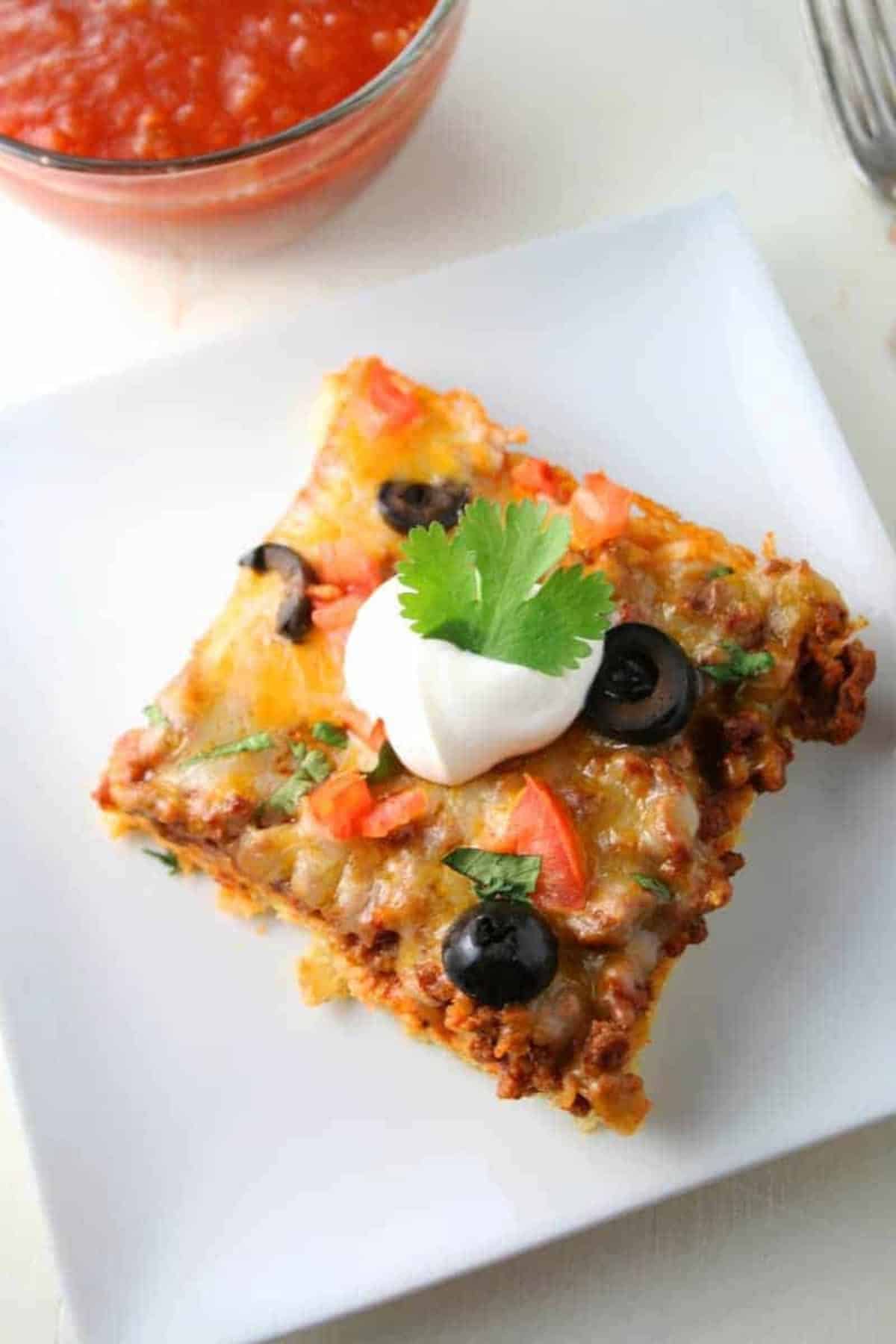 Low Carb Mexican Pizza rectangular slice on white plate. Salsa in the top left corner.