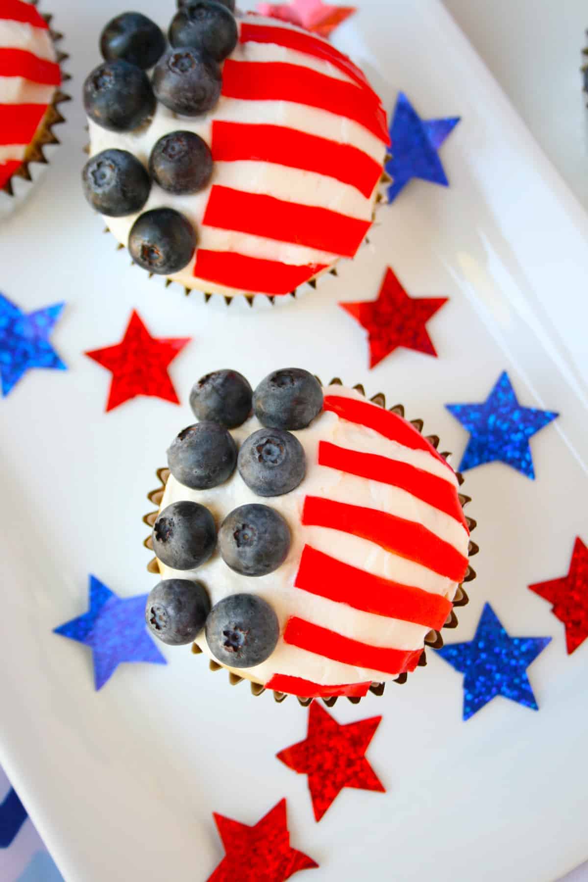 Two flag cupcakes on a white plate with red and blue stars on the plate.