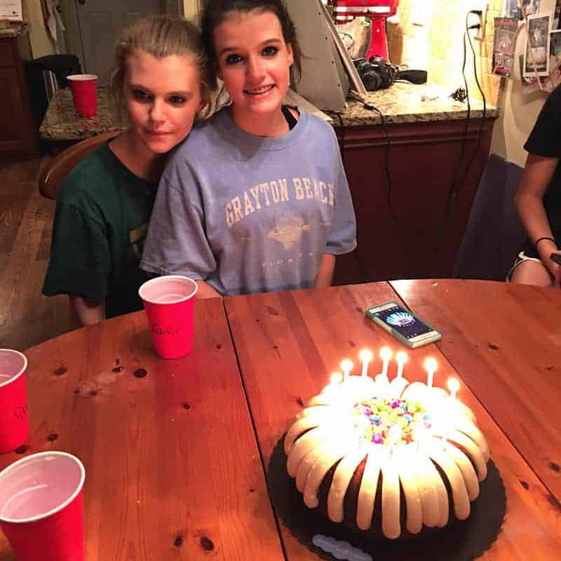 my daughter savannah and friend sitting at a table with a birthday bundt cake with lit candles.
