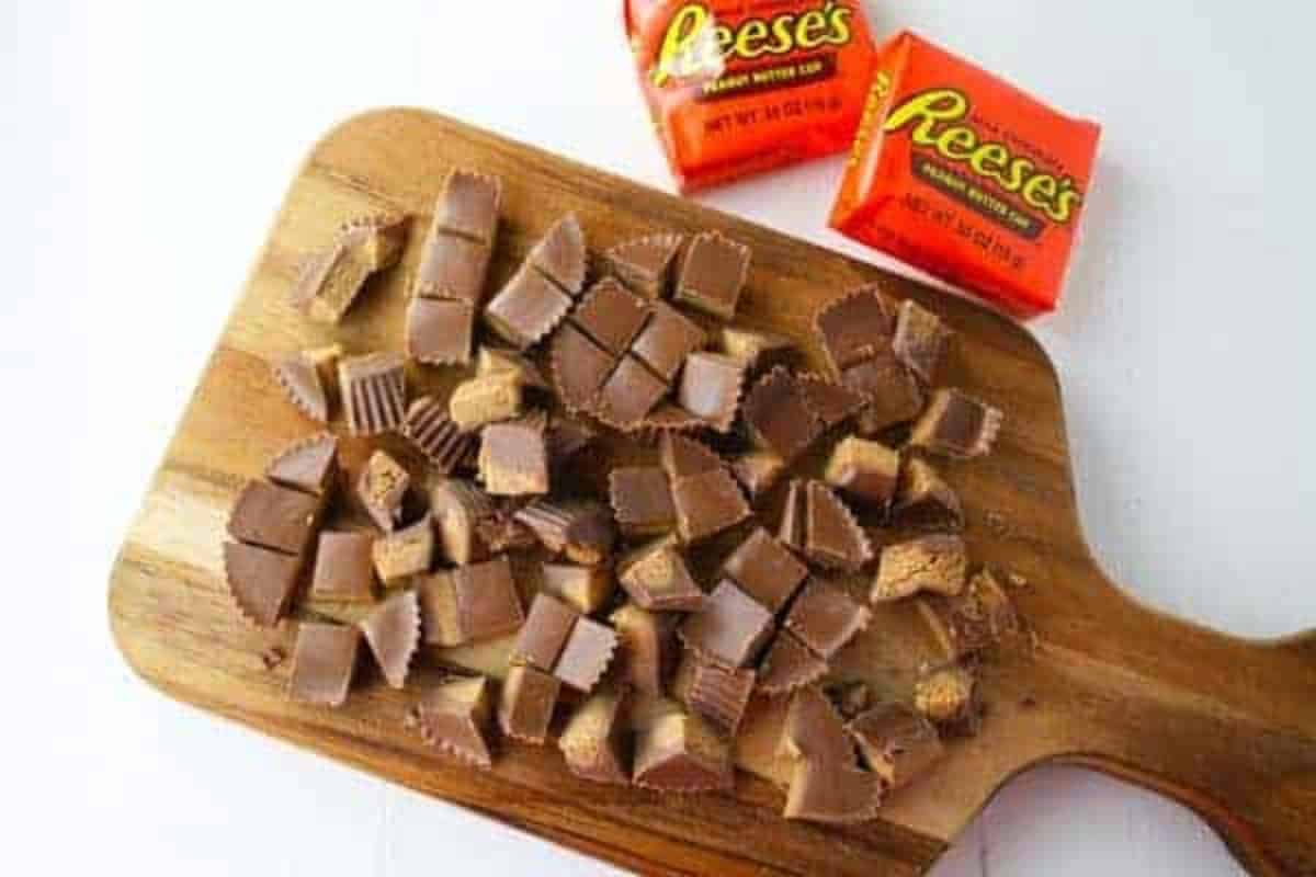 Reeses cups chopped up on a wooden cutting board with two Reeses cups on their packaging.