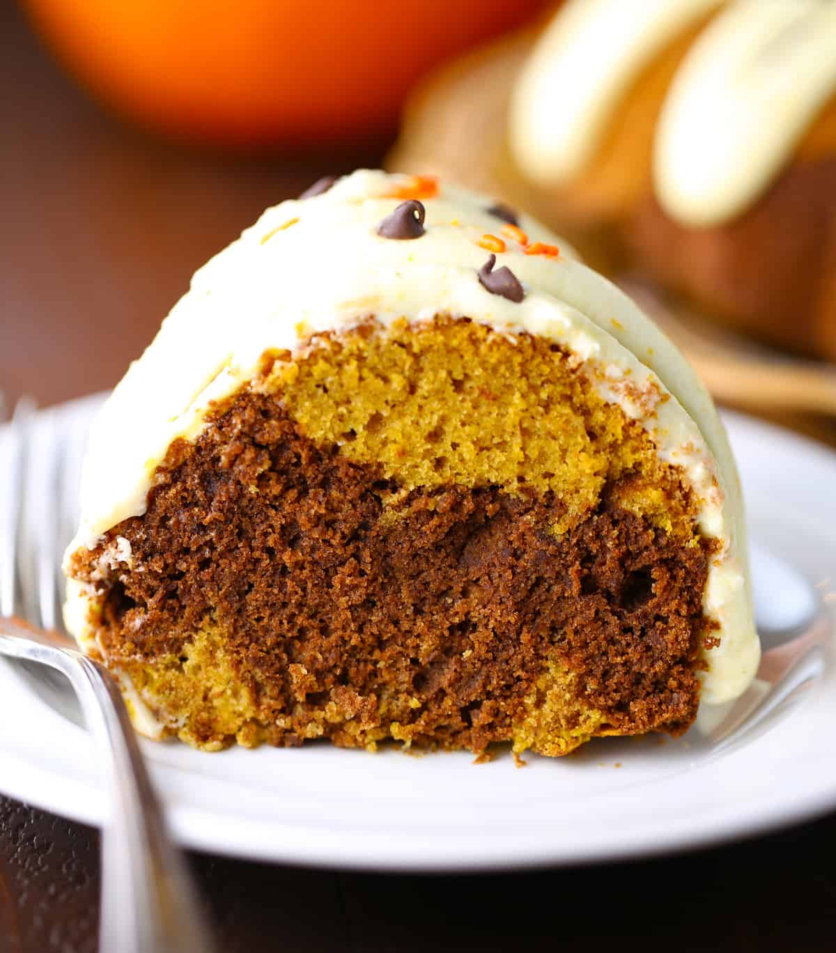 Slice of pumpkin swirl bundt cake on white plate with fork.