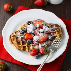 French toast waffle on a white plate with berries, powdered sugar and fork.