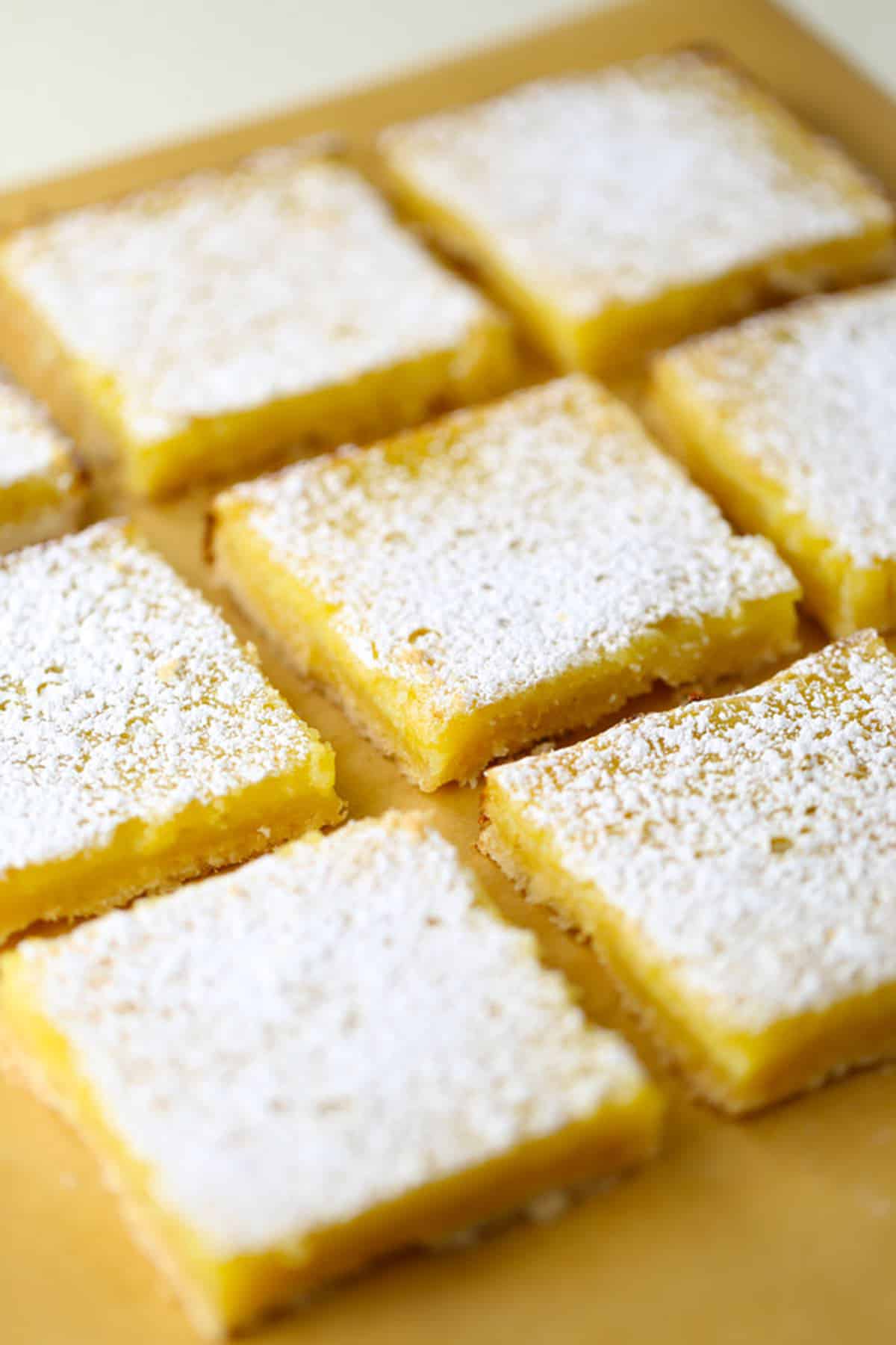 Eight lemon bars on parchment paper with powdered sugar.