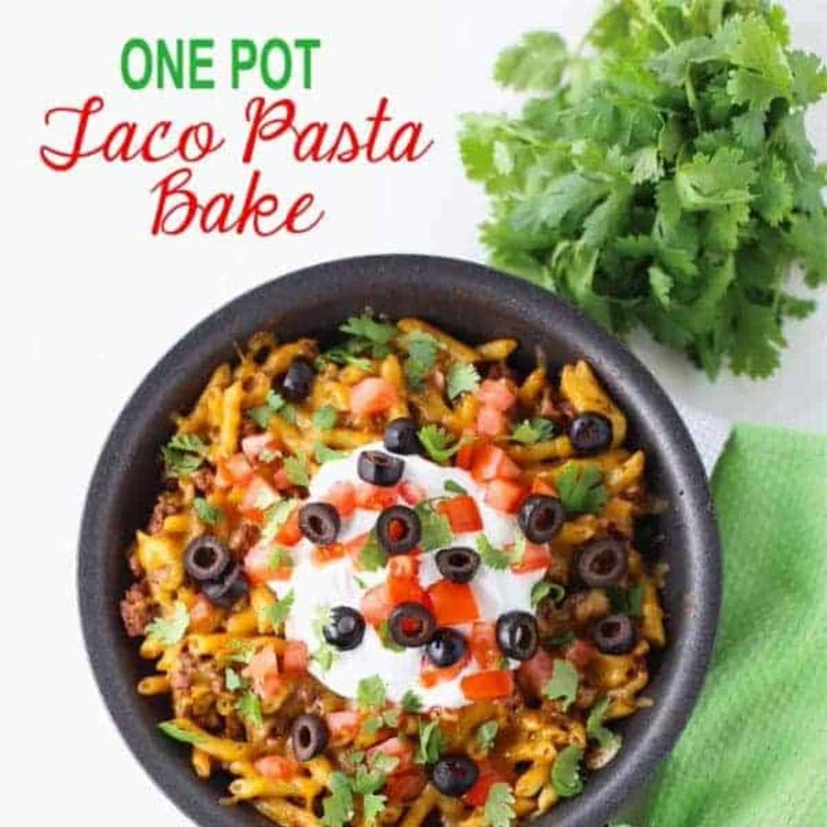 finished taco pasta bake in fry pan with green napkin under bottom right corner of pan. Bundle of parsley in the top right corner. Words One Pot Taco Bake in top left corner. 