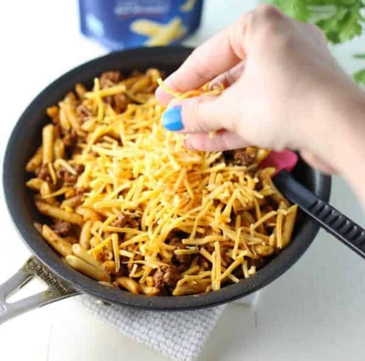 shredded cheese being sprinkled on ground meat in a fry pan. 