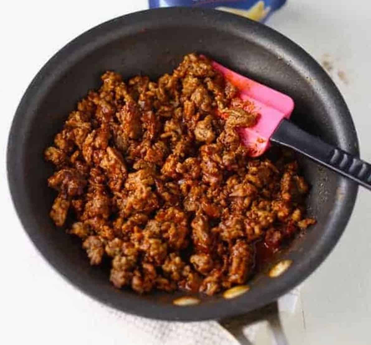 seasoned ground meat in a fry pan being stirred by a spatula.