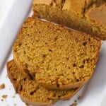Pumpkin bread on white plate with two slices laying down.