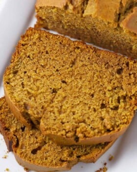 Pumpkin bread on white plate with two slices laying down.