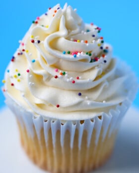 One yellow cake cupcake with a swirl of vanilla frosting and sprinkles on top.