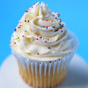 One yellow cake cupcake with a swirl of vanilla frosting and sprinkles on top.