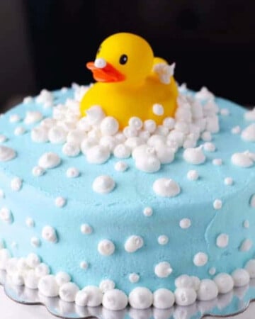 rubber ducky on stop of a blue cake with white frosting for bubbles