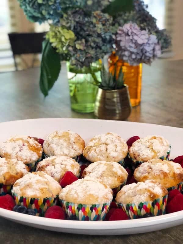 White chocolate raspberry muffins on a white plate with flowers on table.