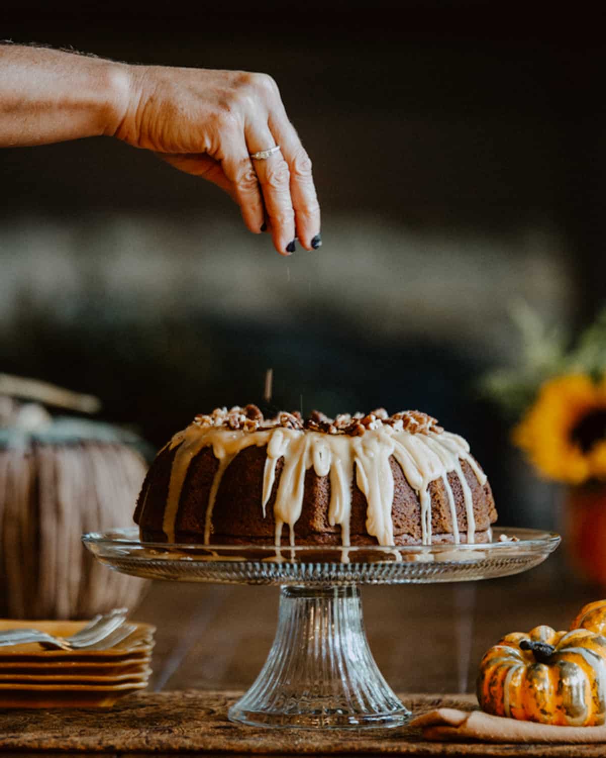 Pumpkin bundt cake on a glass cake stand with flowers in the background.