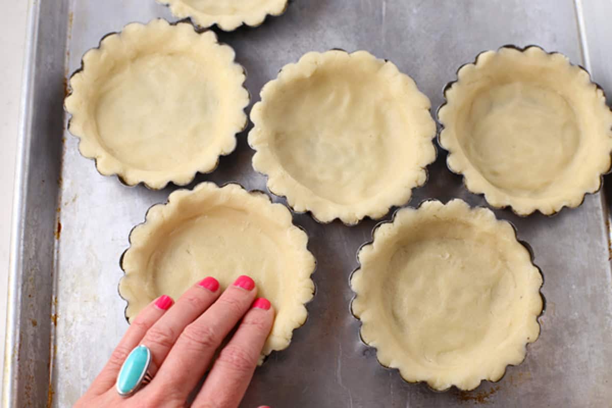 Shortbread crust in mini tart tins on a cookie sheet.