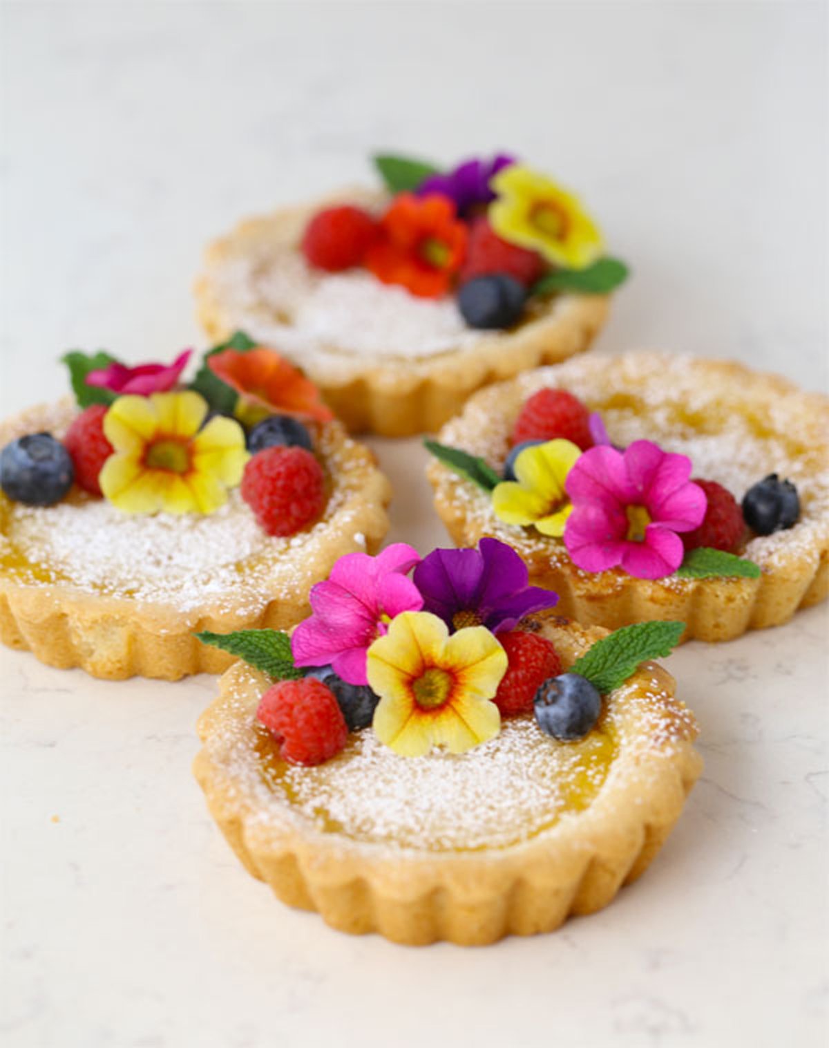 Beautifully presented lemon tarts with edible flowers on top.
