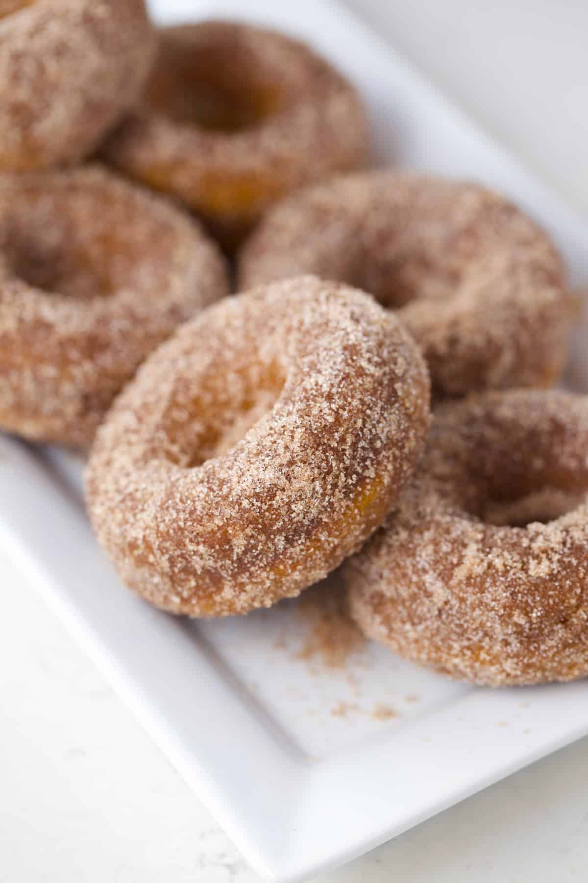 Pumpkin donuts piled high on a white plate.