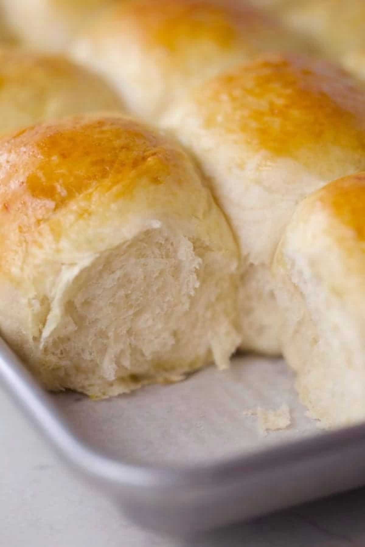 a closeup of golden brown homemade dinner rolls with one missing from the pan.