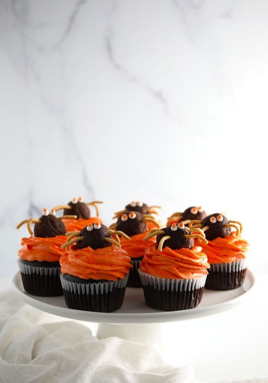 Chocolate cupcakes with vanilla buttercream frosting colored orange for Halloween topped with a chocolate truffle spider with chow mein noodle legs.