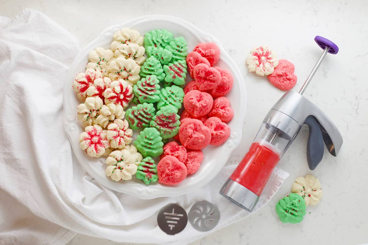 Cookie press and white plate with baked cookies.