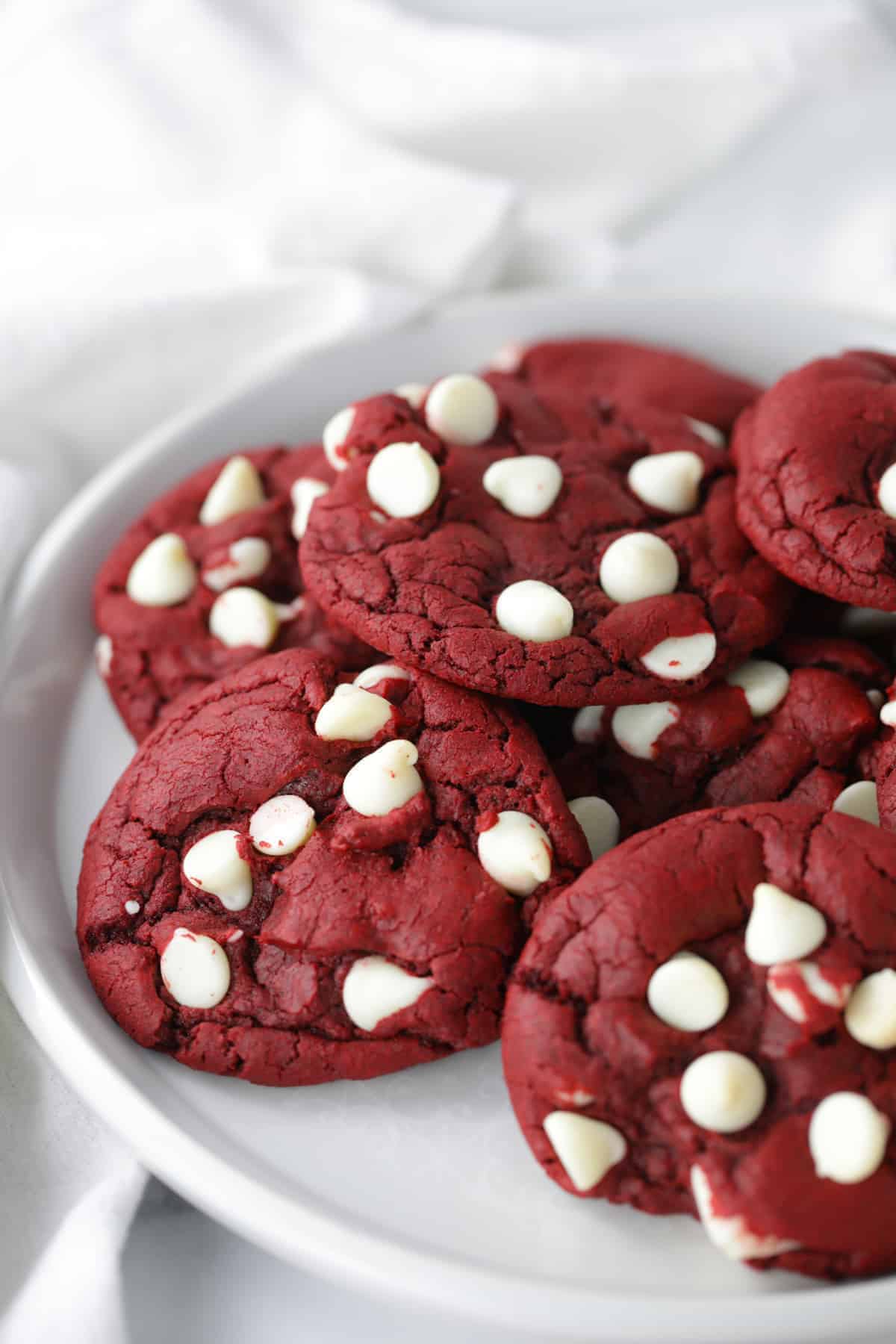 Ten red velvet cookies piled on a white plate.