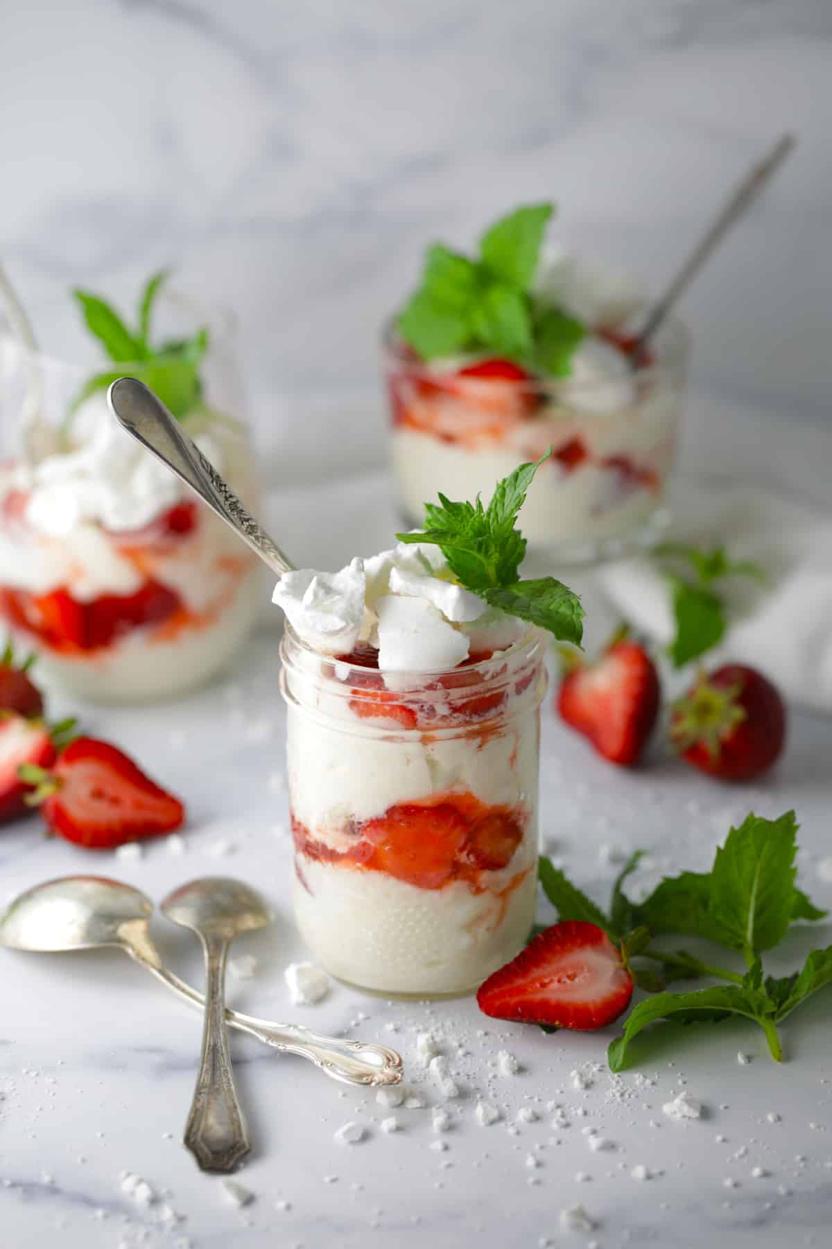 Eton mess in mason jars on the counter with spoons and berries strewn about.