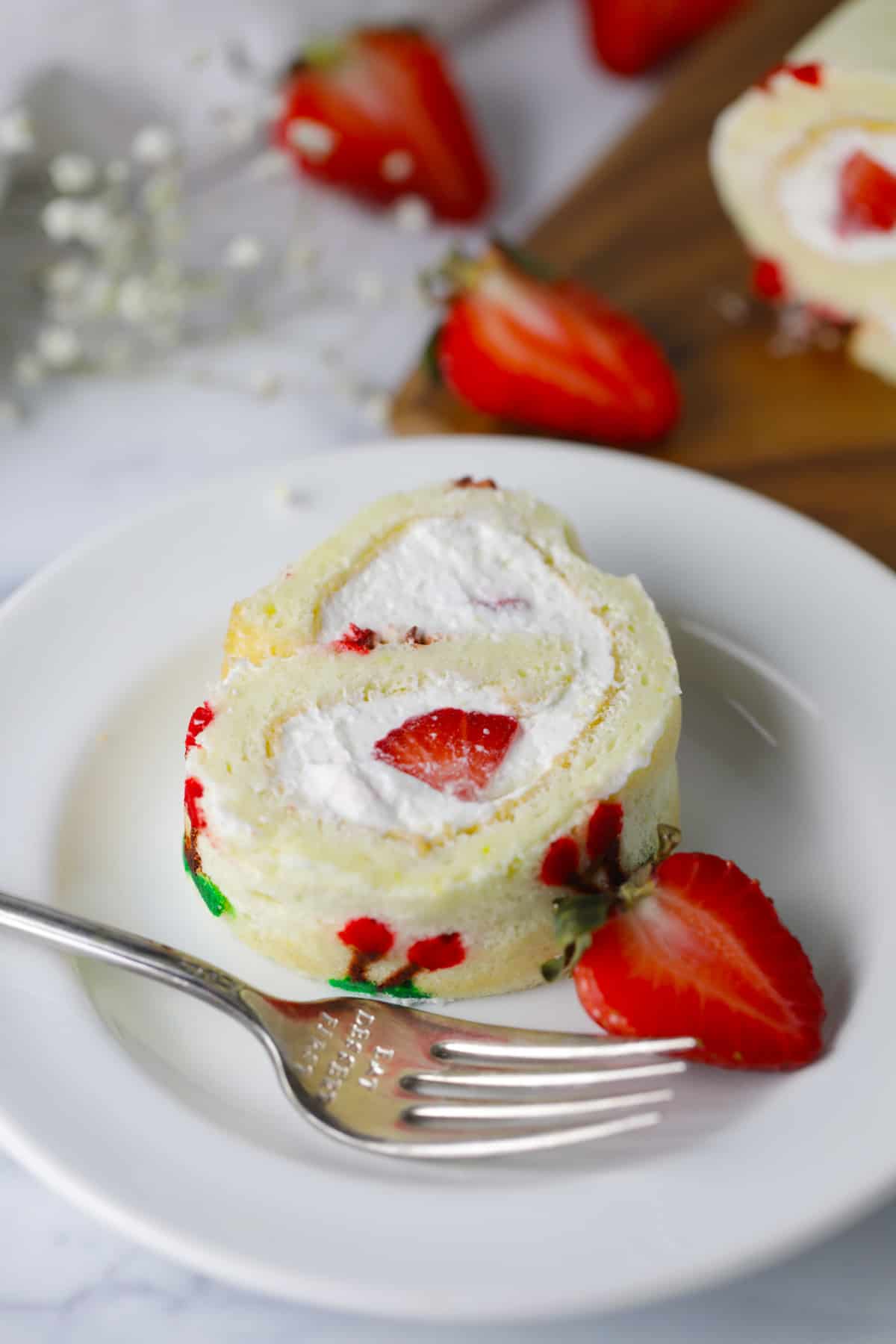 Slice of cake roll with whipped cream and fresh strawberries.