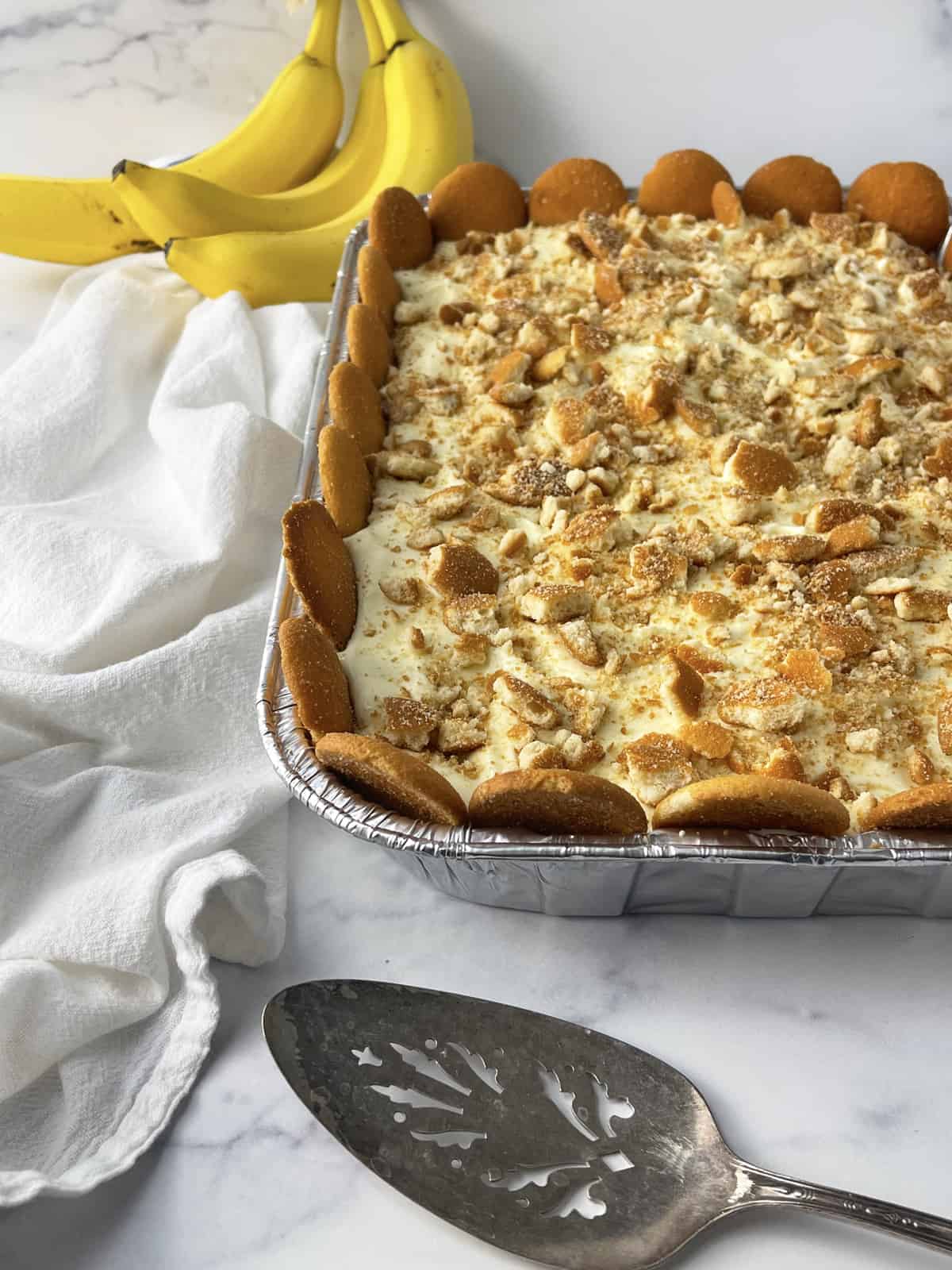 Large pan of banana pudding with bananas in the background and serving spoon.