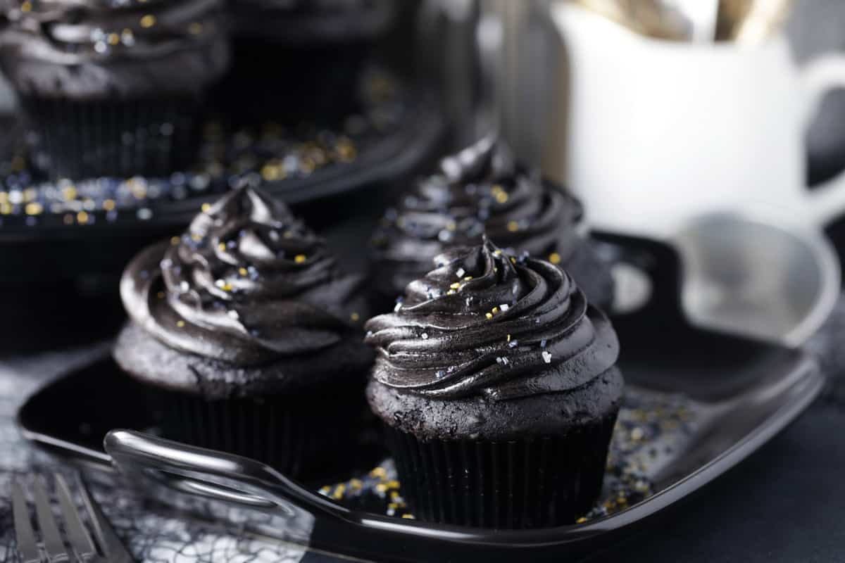 Three black frosted cupcakes on a black plate.