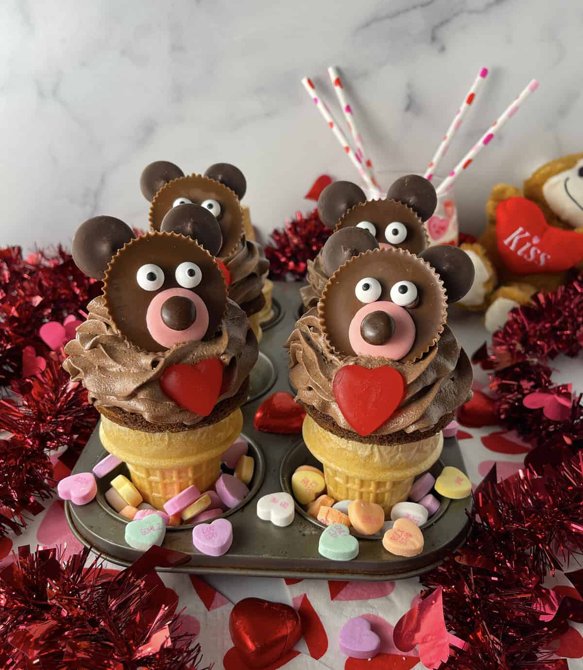 Muffin pan with four decorated teddy bear cupcakes and candy on the sides.
