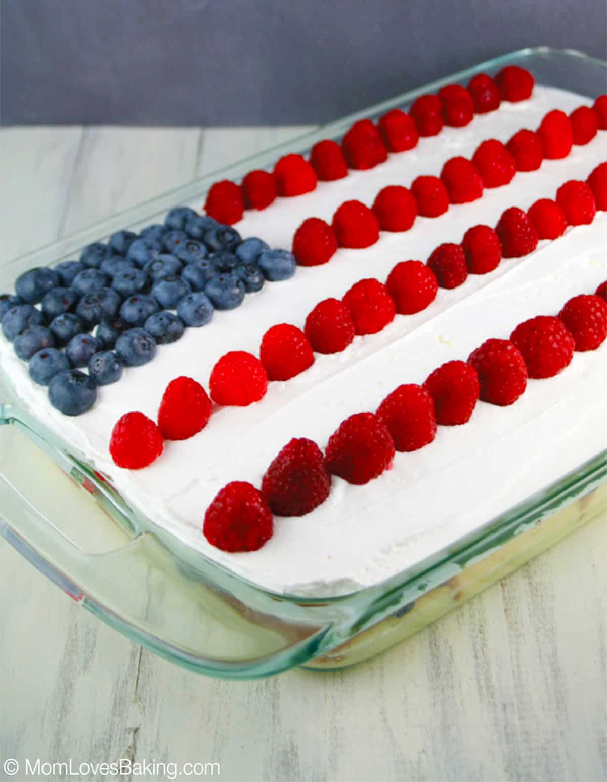 Clear glass casserole dish with layered dessert frosted with cool whip and flag design made of berries.