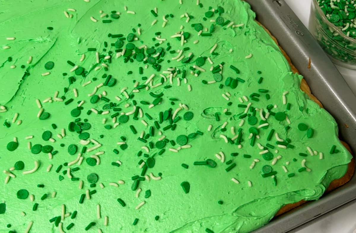 Sugar cookie bars in sheet pan with green frosting.