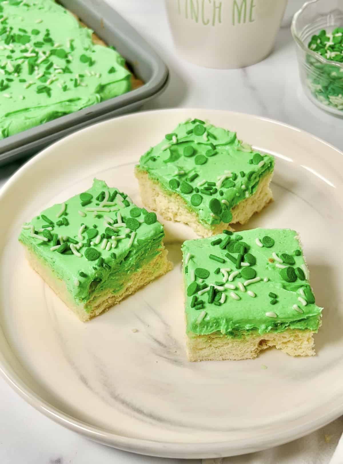 Sugar cookie bars with green frosting on a white plate.