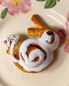 Bunny shaped cinnamon roll on a flowered plate.
