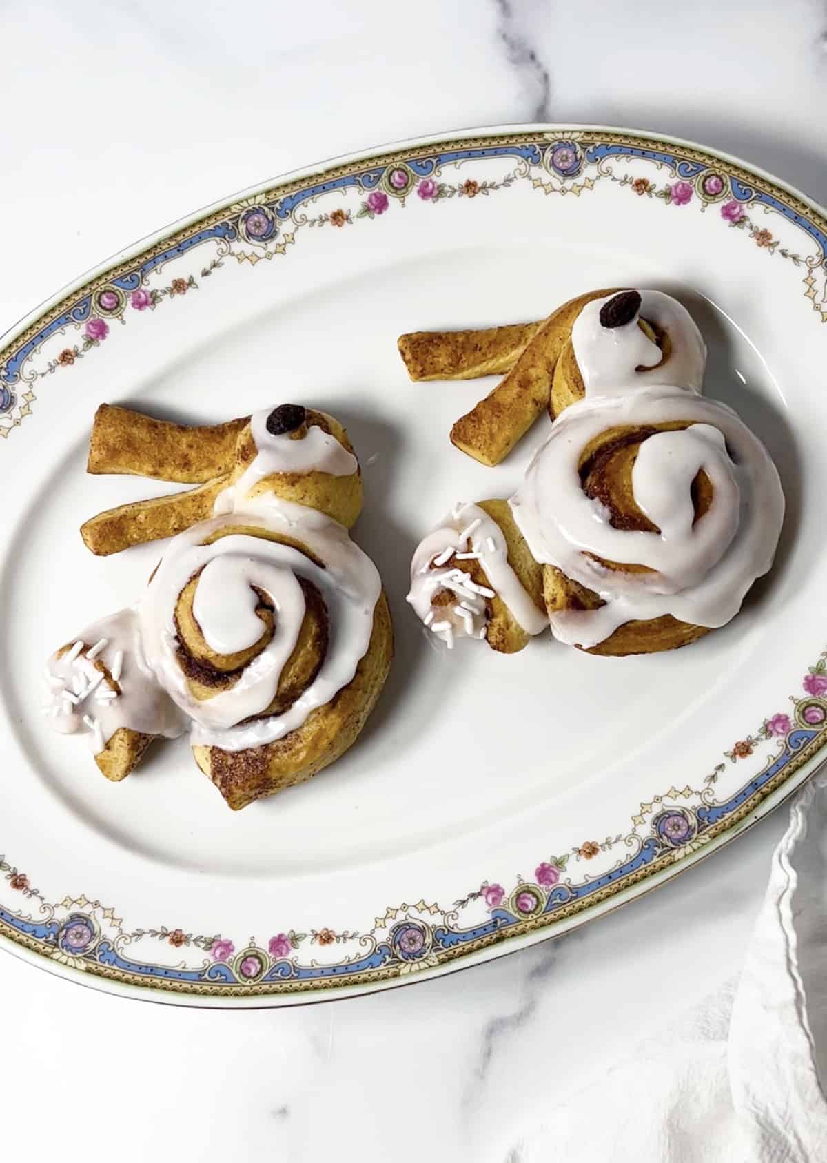 Two bunny shaped cinnamon rolls on a pretty floral plate.