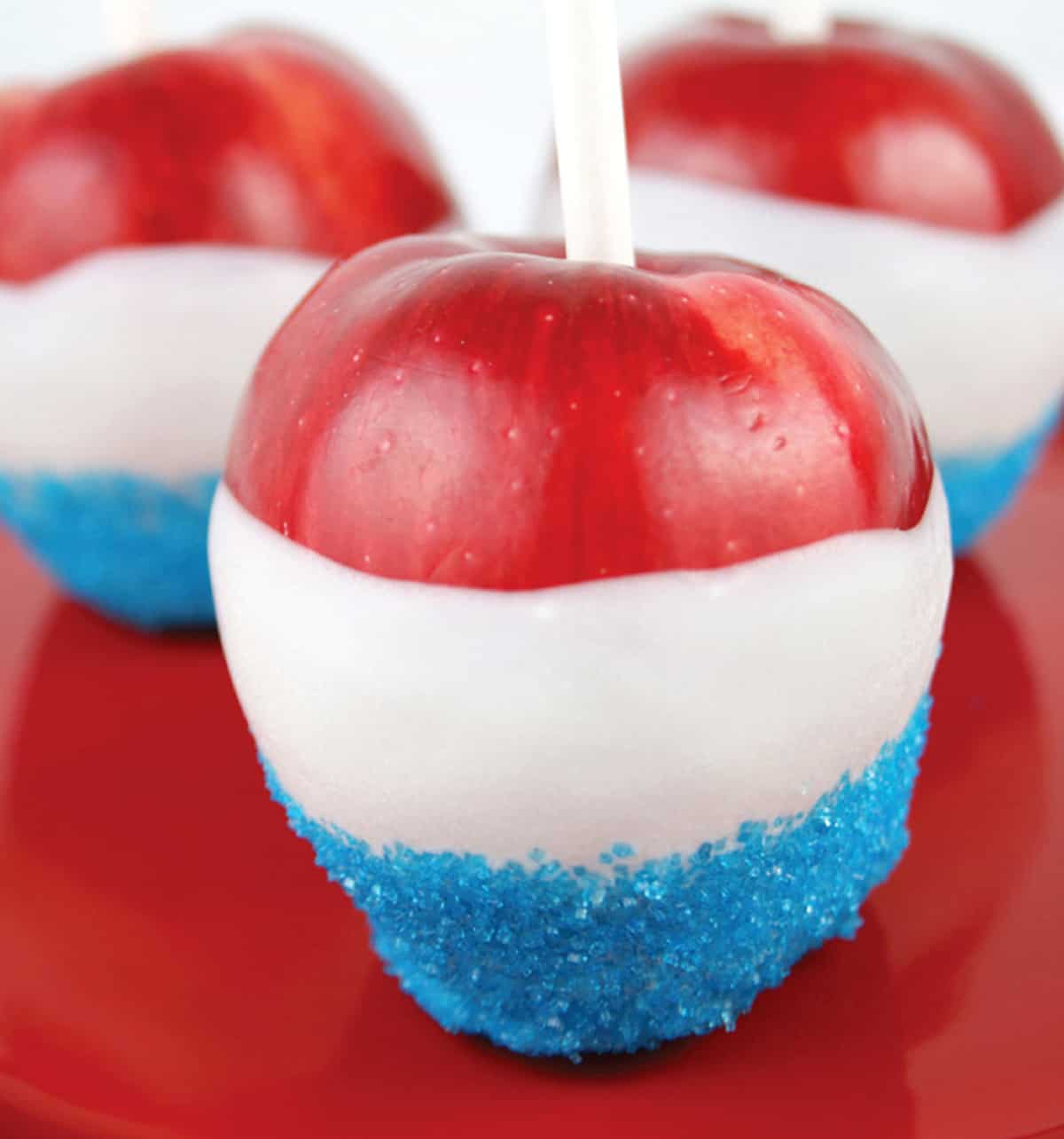 Red apples on a stick dipped in white chocolate and blue sprinkles.