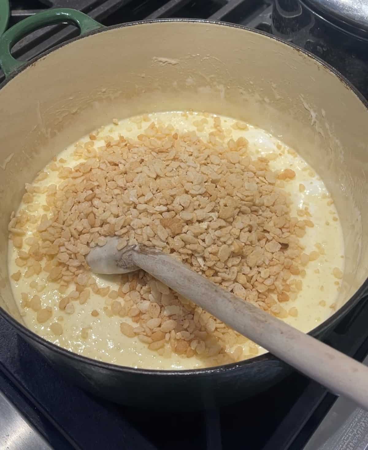 Adding rice cereal to melted butter and marshmallows in saucepan.