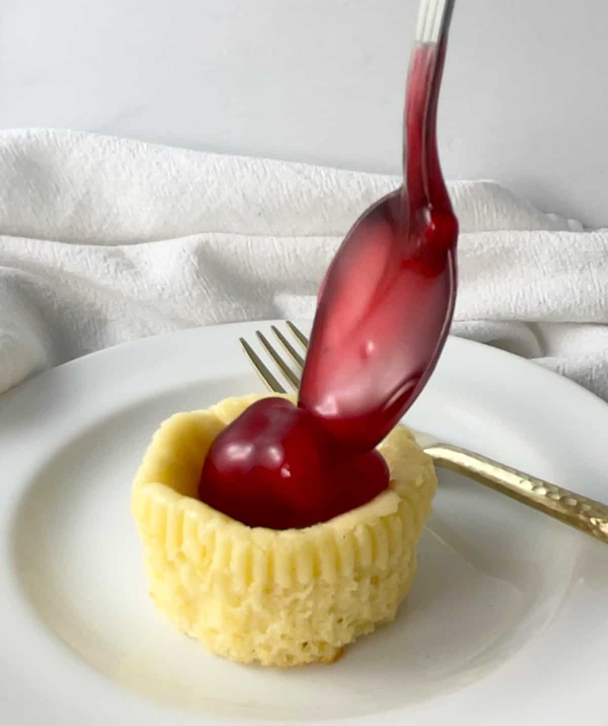 Spooning cherry pie filling on top of a mini cheesecake cupcake.